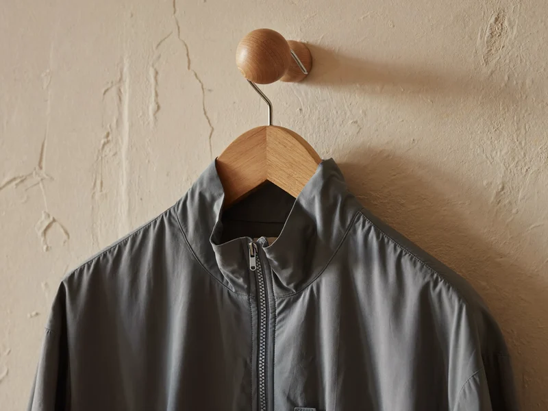 Giacca leggera con zip appesa a un gancio di legno su parete in intonaco