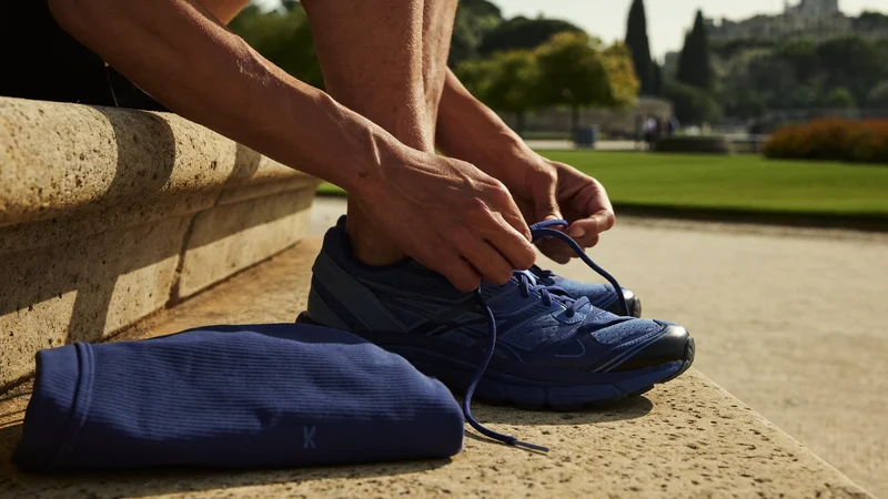 Mani che allacciano le scarpe da corsa accanto a un top piegato in un parco